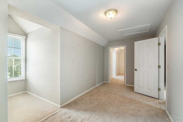 carpeted spare room featuring attic access, vaulted ceiling, and baseboards