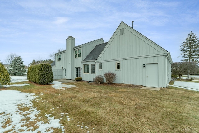 back of house with a shingled roof, a chimney, a lawn, and board and batten siding