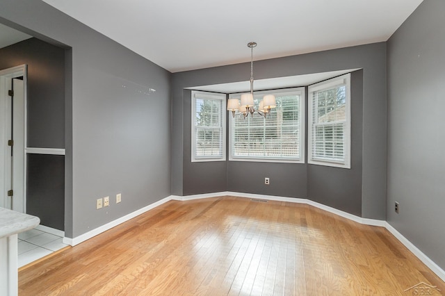 empty room featuring baseboards, a chandelier, and hardwood / wood-style floors