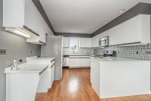 kitchen featuring a peninsula, light countertops, appliances with stainless steel finishes, backsplash, and light wood finished floors