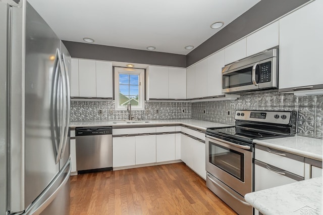 kitchen with stainless steel appliances, light countertops, white cabinetry, a sink, and wood finished floors