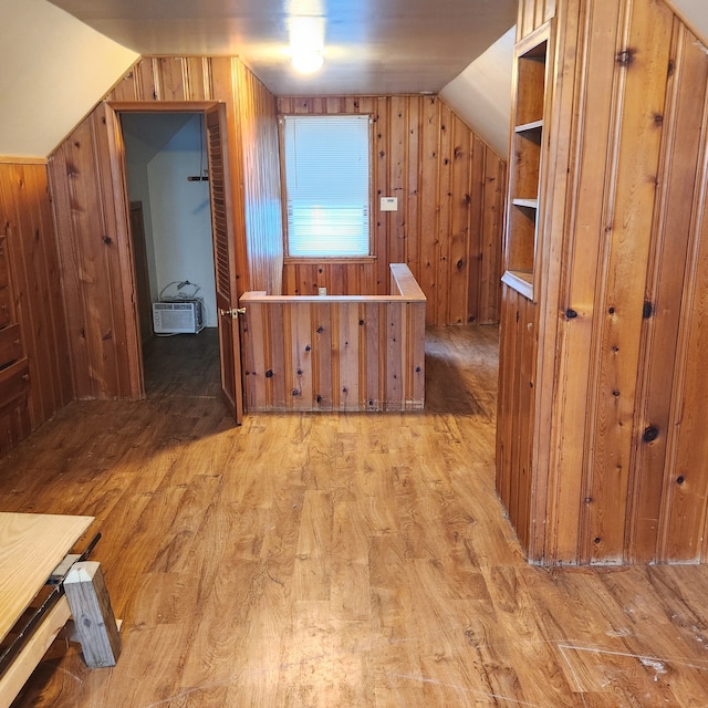 hall featuring lofted ceiling, wooden walls, a wall unit AC, and light wood-type flooring