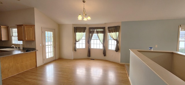 unfurnished dining area featuring vaulted ceiling, sink, an inviting chandelier, and light hardwood / wood-style flooring