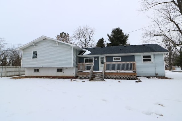 snow covered back of property featuring fence and a deck