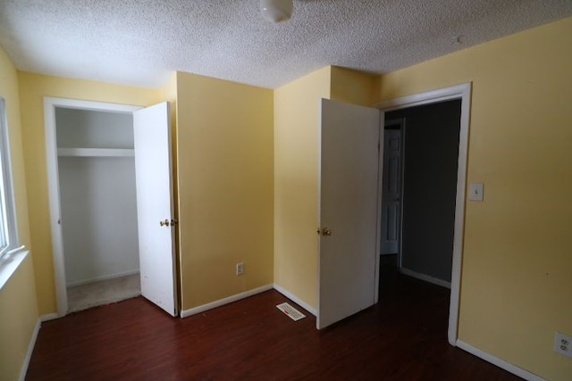 unfurnished bedroom featuring baseboards, a textured ceiling, visible vents, and dark wood-type flooring