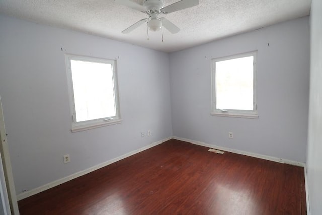 spare room with dark wood-style floors, a wealth of natural light, a textured ceiling, and baseboards