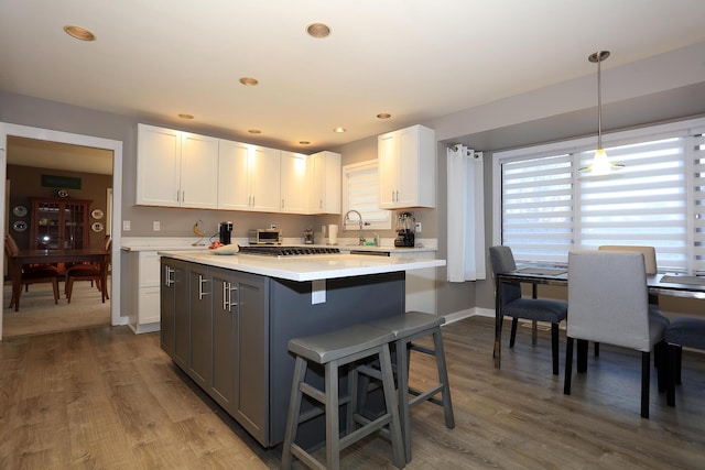 kitchen featuring sink, white cabinetry, hanging light fixtures, hardwood / wood-style floors, and a kitchen bar