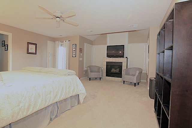 bedroom featuring light carpet, vaulted ceiling, a tile fireplace, and ceiling fan