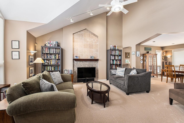 carpeted living room with ceiling fan, track lighting, high vaulted ceiling, and a tile fireplace