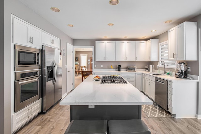 kitchen with sink, white cabinetry, a center island, light wood-type flooring, and appliances with stainless steel finishes