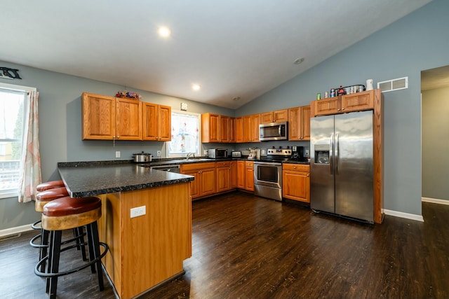 kitchen featuring lofted ceiling, a breakfast bar area, appliances with stainless steel finishes, dark hardwood / wood-style flooring, and kitchen peninsula