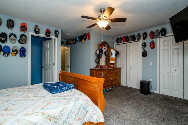 carpeted bedroom featuring multiple closets, a textured ceiling, and ceiling fan