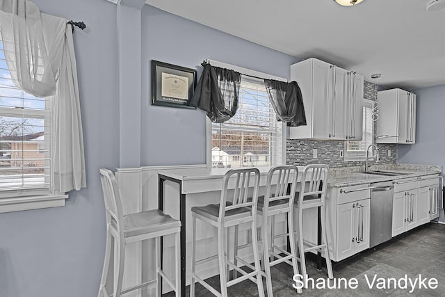 kitchen featuring sink, dishwasher, white cabinetry, tasteful backsplash, and a kitchen bar