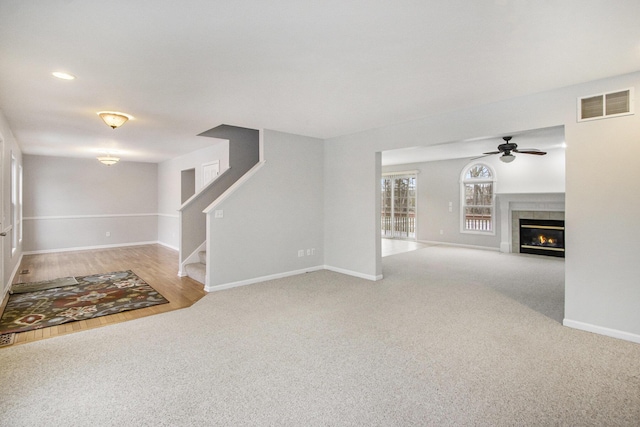 unfurnished living room with a tile fireplace, light colored carpet, and ceiling fan