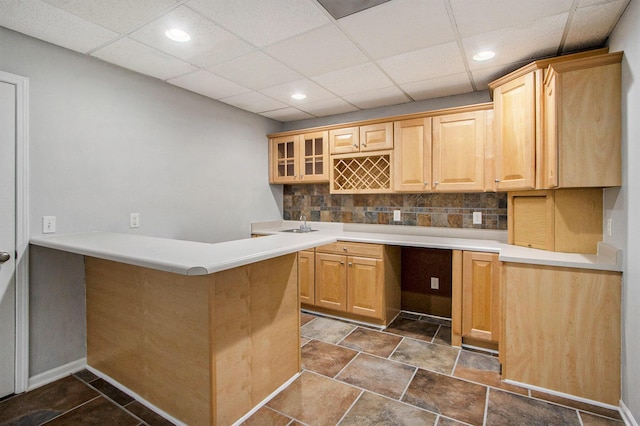 kitchen with backsplash, kitchen peninsula, a drop ceiling, and light brown cabinets