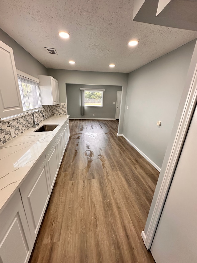 kitchen with tasteful backsplash, sink, white cabinets, light hardwood / wood-style floors, and light stone countertops