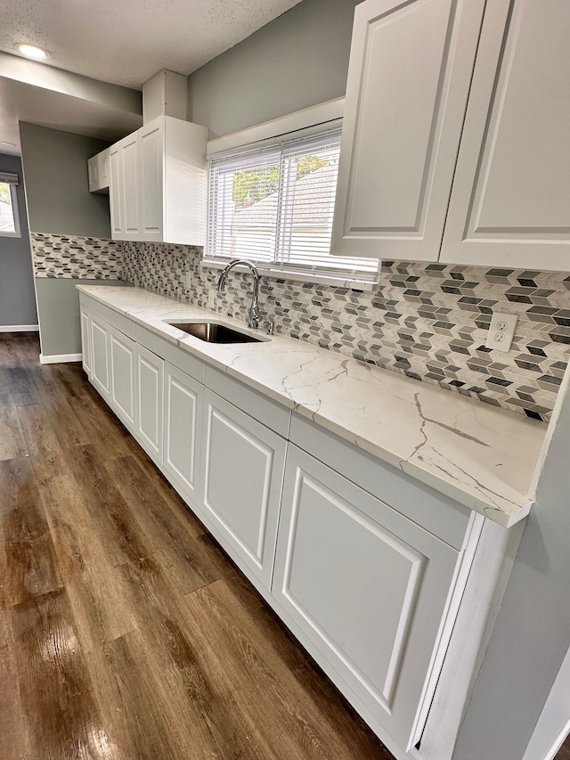 kitchen with sink, white cabinetry, light stone counters, dark hardwood / wood-style floors, and backsplash