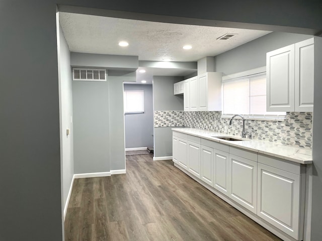 kitchen with sink, hardwood / wood-style flooring, white cabinetry, a textured ceiling, and decorative backsplash