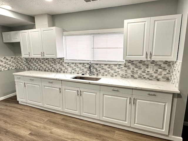 kitchen featuring white cabinetry, sink, decorative backsplash, light stone counters, and light wood-type flooring