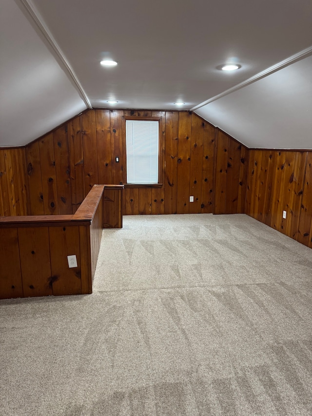 bonus room featuring vaulted ceiling, light colored carpet, and wood walls