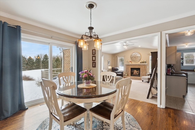 dining space featuring hardwood / wood-style floors, a fireplace, lofted ceiling, sink, and ornamental molding