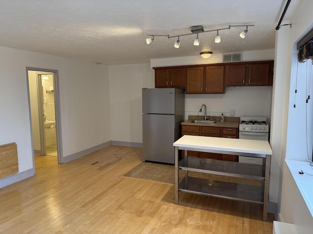 kitchen with sink, stainless steel refrigerator, a textured ceiling, and light wood-type flooring