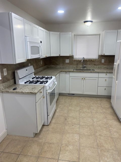 kitchen featuring light stone countertops, sink, white cabinets, and white appliances