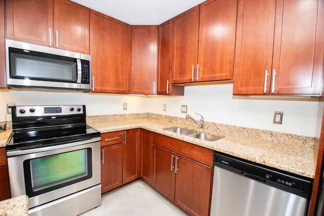 kitchen featuring stainless steel appliances, light stone counters, brown cabinetry, and a sink