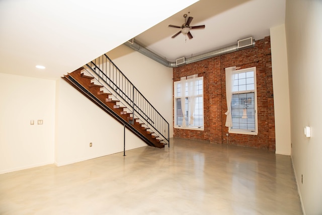 unfurnished living room featuring visible vents, a high ceiling, a ceiling fan, brick wall, and concrete flooring