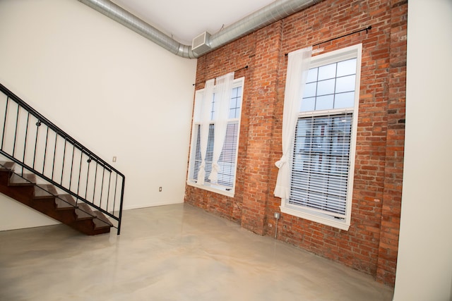 empty room featuring stairs, brick wall, and finished concrete floors