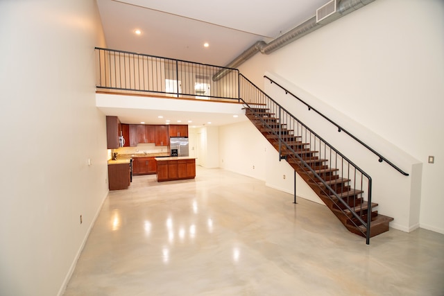 living room with finished concrete flooring, stairway, a towering ceiling, and baseboards