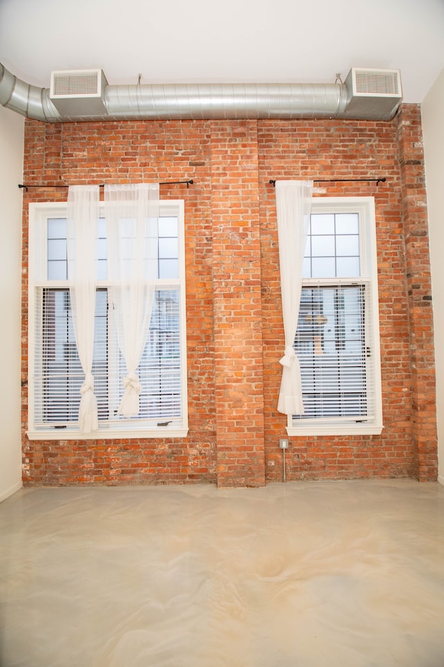 unfurnished room with brick wall, visible vents, and concrete flooring