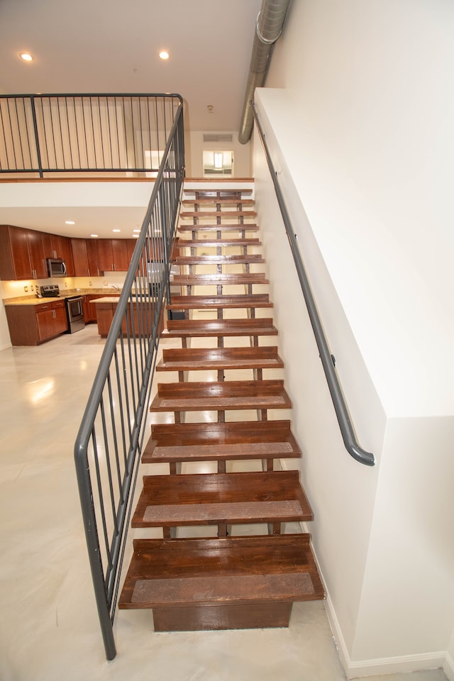 stairway featuring recessed lighting, a towering ceiling, and baseboards