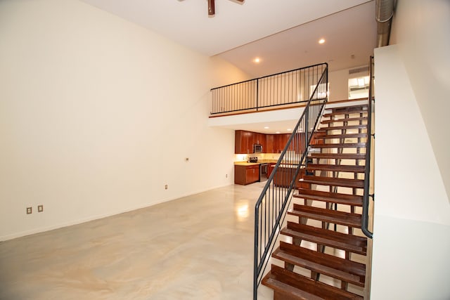 staircase with concrete floors, recessed lighting, a towering ceiling, and baseboards