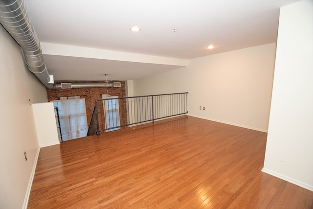 spare room with brick wall, baseboards, wood finished floors, and recessed lighting