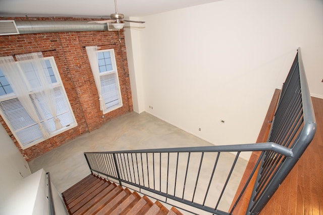 stairs with visible vents, brick wall, concrete floors, and a ceiling fan