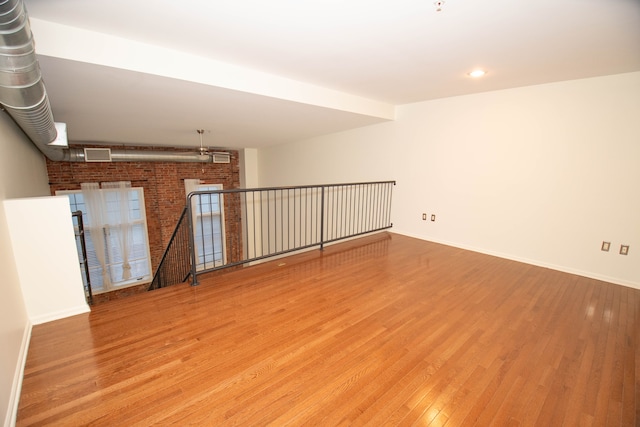 spare room featuring brick wall, wood finished floors, visible vents, and baseboards