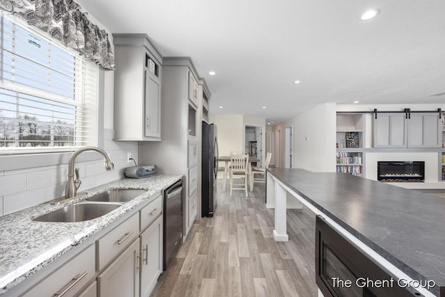 kitchen with sink, gray cabinetry, stainless steel dishwasher, black fridge, and light wood-type flooring