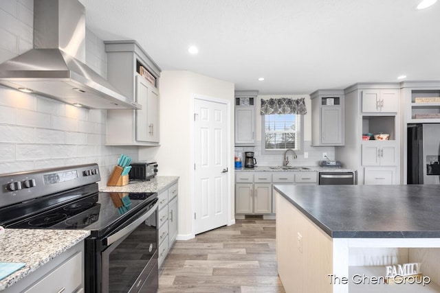 kitchen featuring sink, appliances with stainless steel finishes, gray cabinets, light hardwood / wood-style floors, and wall chimney range hood