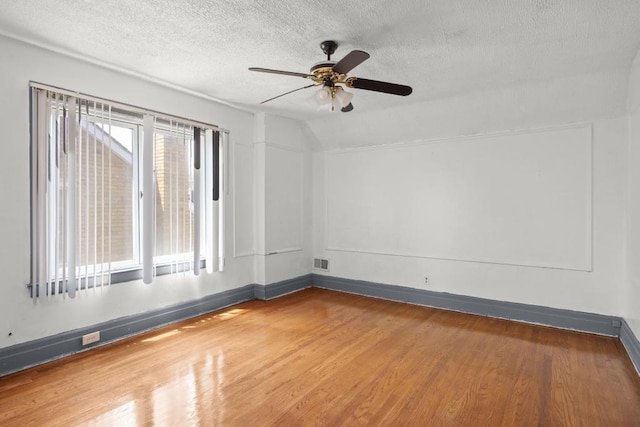 empty room with vaulted ceiling, ceiling fan, hardwood / wood-style floors, and a textured ceiling