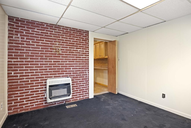 unfurnished living room with dark colored carpet, brick wall, heating unit, and a drop ceiling