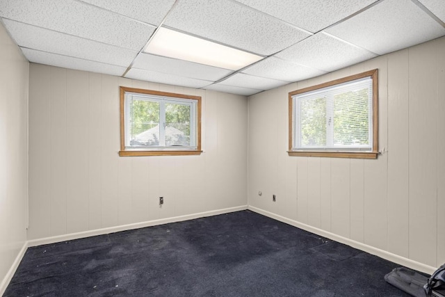 unfurnished room featuring dark colored carpet, a healthy amount of sunlight, and a paneled ceiling