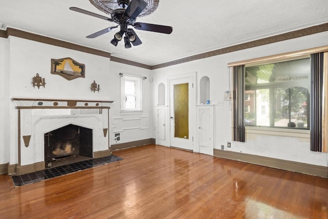 unfurnished living room featuring a fireplace, wood-type flooring, ornamental molding, and ceiling fan