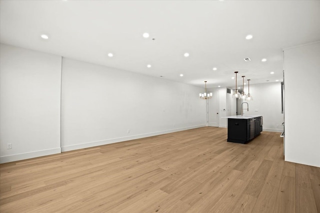 unfurnished living room with an inviting chandelier, sink, and light wood-type flooring