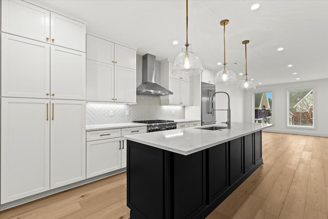 kitchen with pendant lighting, sink, white cabinets, a kitchen island with sink, and wall chimney exhaust hood