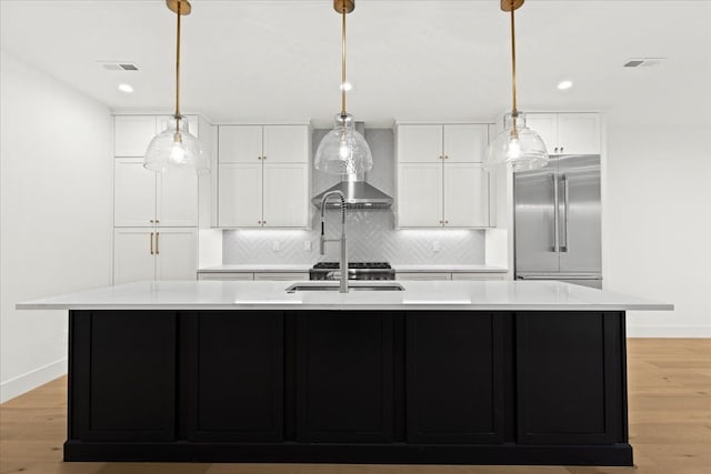 kitchen featuring light hardwood / wood-style flooring, built in refrigerator, white cabinets, and a center island with sink