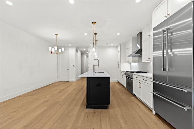 kitchen with pendant lighting, sink, wall chimney range hood, high end appliances, and a center island with sink