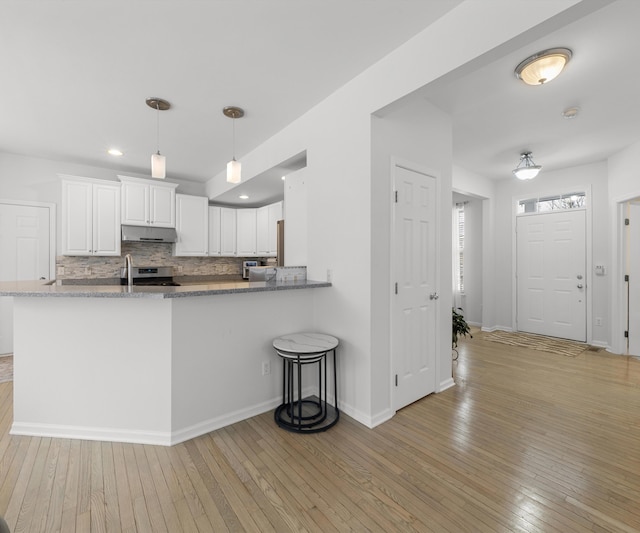 kitchen with backsplash, hanging light fixtures, light hardwood / wood-style floors, white cabinets, and kitchen peninsula