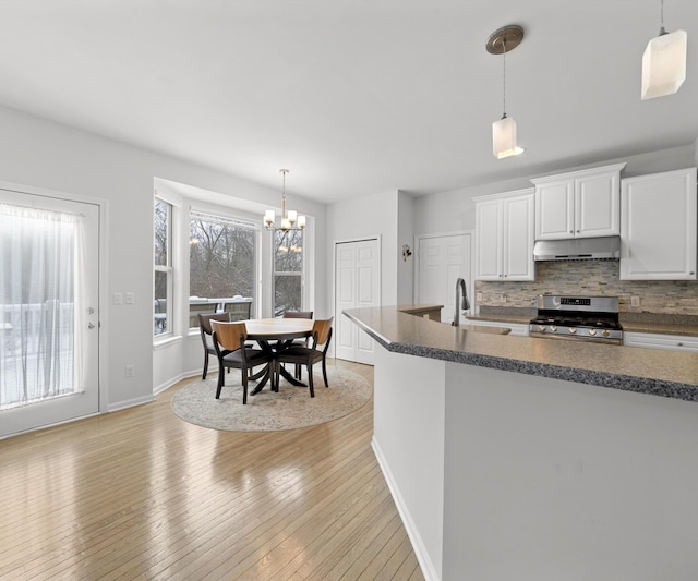 kitchen with pendant lighting, backsplash, light hardwood / wood-style floors, white cabinets, and stainless steel range oven