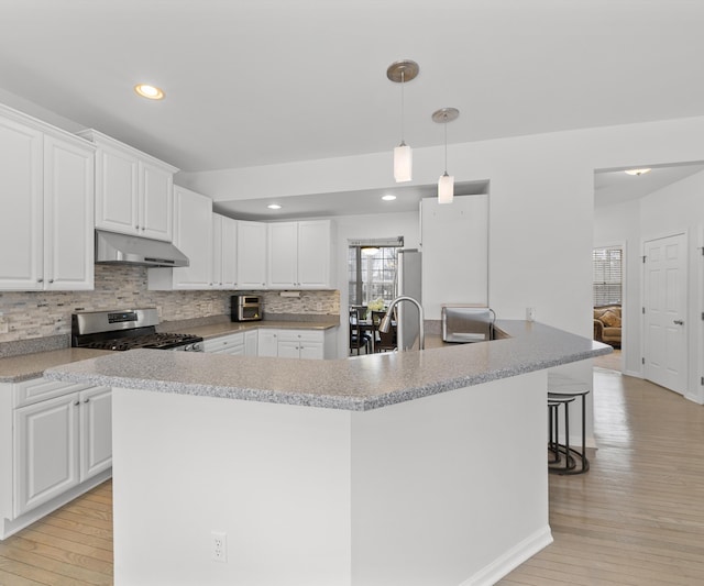 kitchen featuring stainless steel gas stove, decorative light fixtures, light hardwood / wood-style floors, and white cabinets